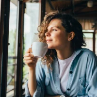 Young women looking out the window with a hot drink.