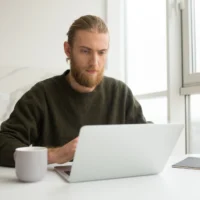 Young man sitting at the table with a cup. He is working.